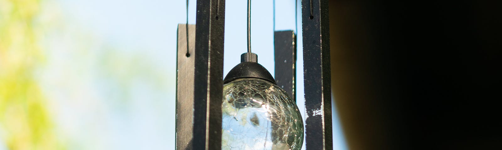 Wind chimes with a glass ball hanging from a roof ledge. A metal butterfly hangs between the chimes.