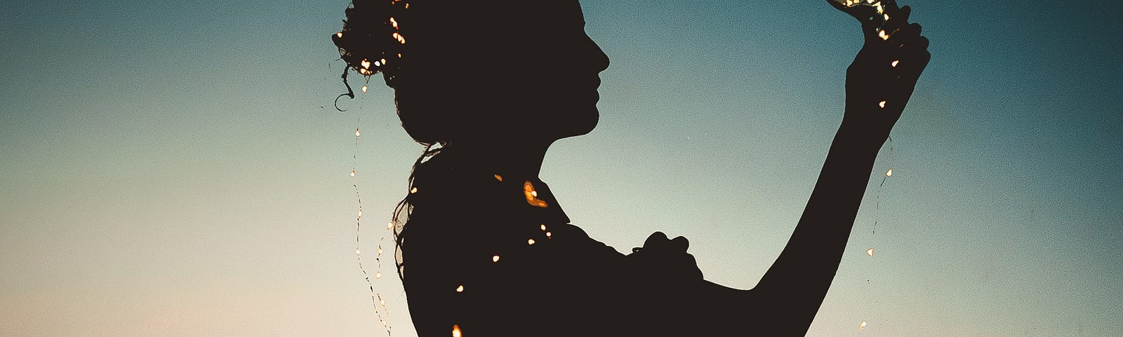 Silhouette of woman holding light bulb against blue and orange sunset backdrop