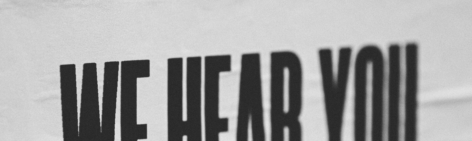 White poster with the words “We hear you” written in black.