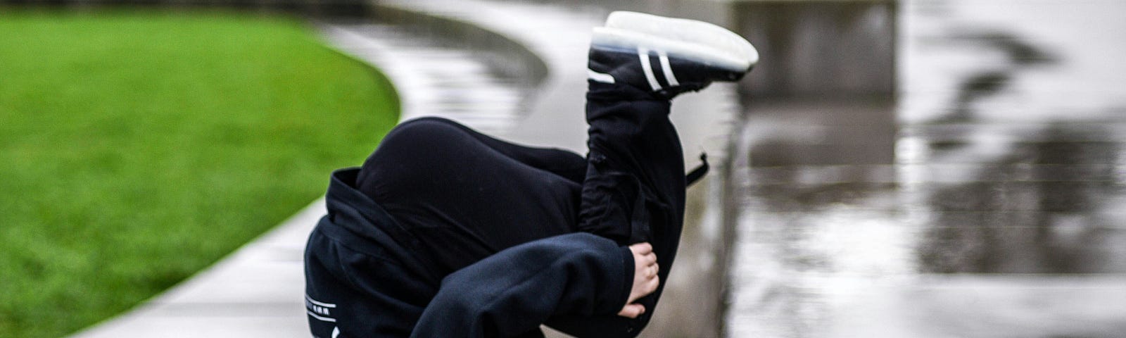 Young person somersaulting on a wet sidewalk