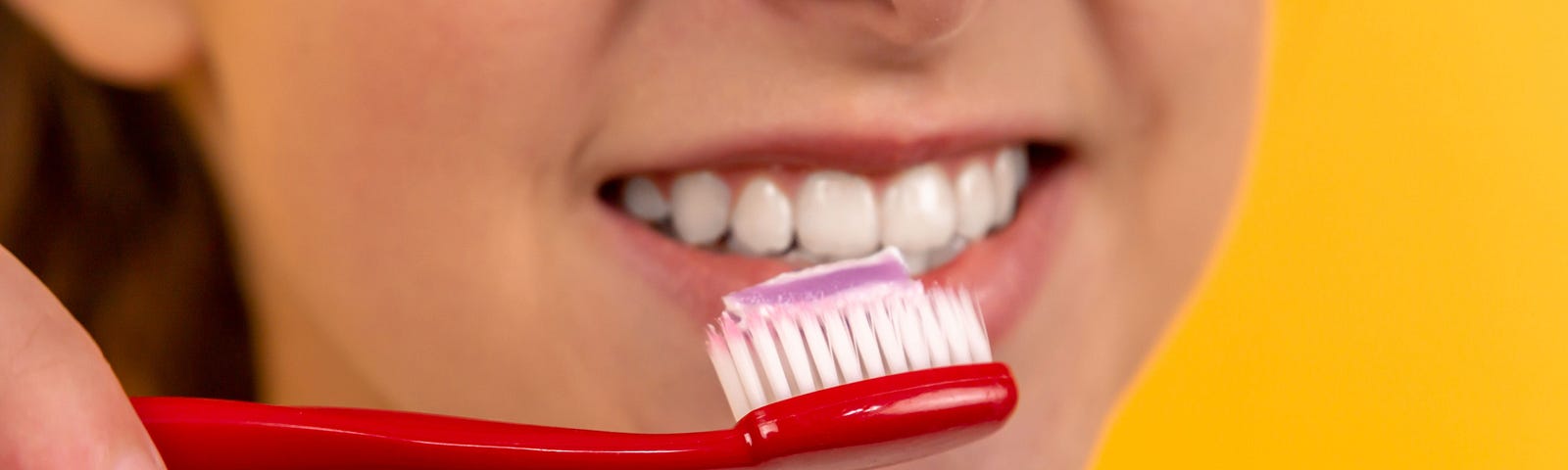A woman, smiling, holding up a toothbrush to her mouth.