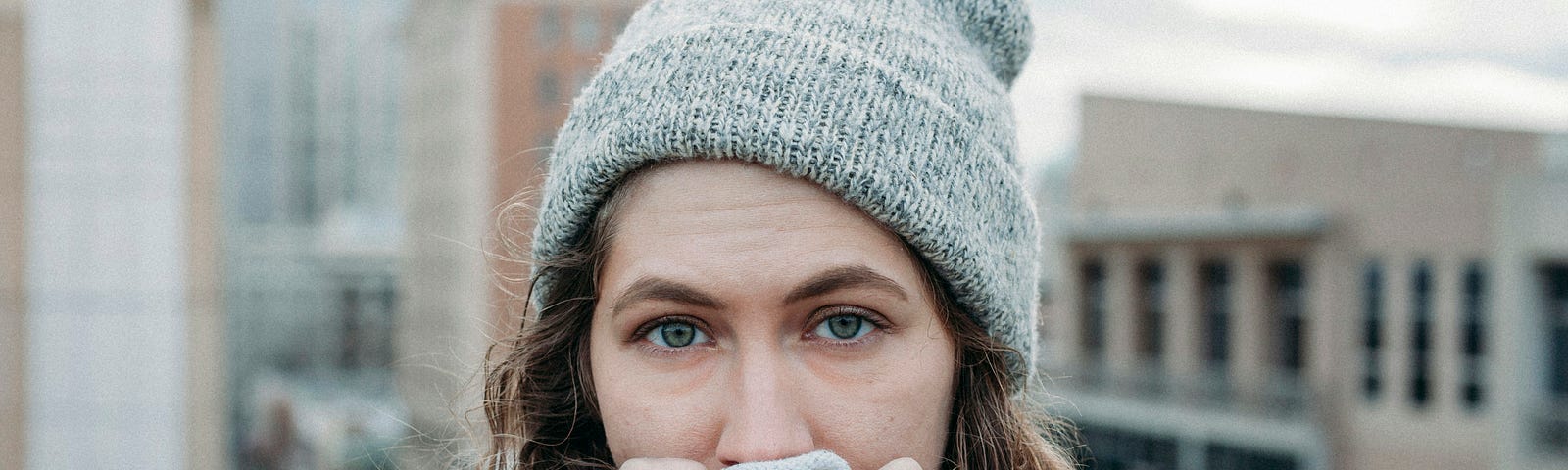 A tired woman wrapped up in a thick coat, beanie, and scarf.