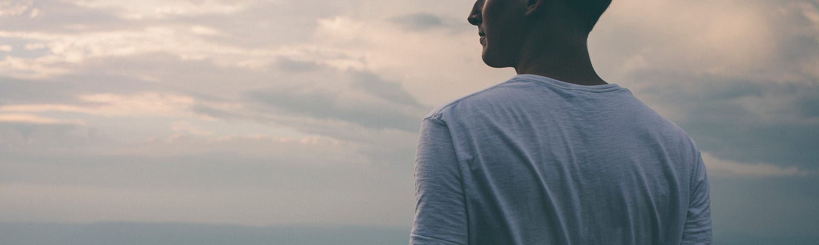 A guy in a white t-shirt looking out on top of a summit.