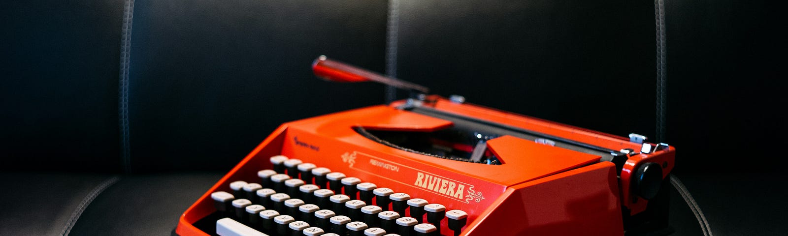 A bright red typewriter sits on a black couch