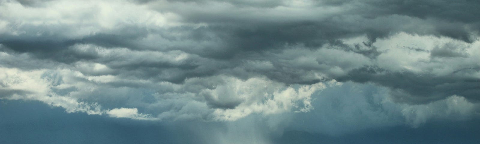 Storm at great distance, viewed over large lake. Swath of rain visible, blowing across horizon.