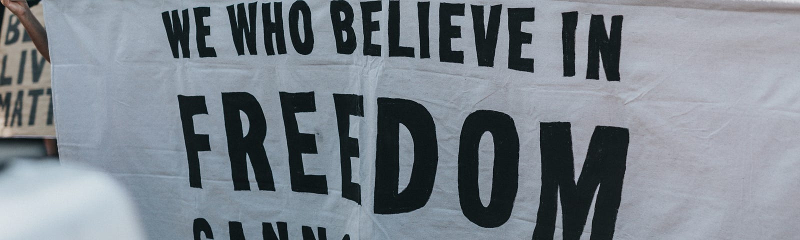 A group of protestors hold up a banner that reads, “We who believe in freedom cannot rest — Ella Baker”