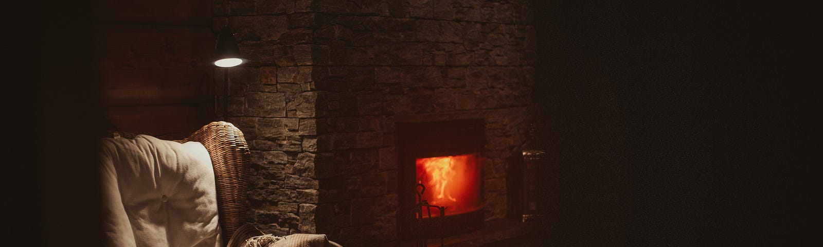 Darkish image of a burning fireplace in the middle of the image, and a chair to the left with a white blanket over it.