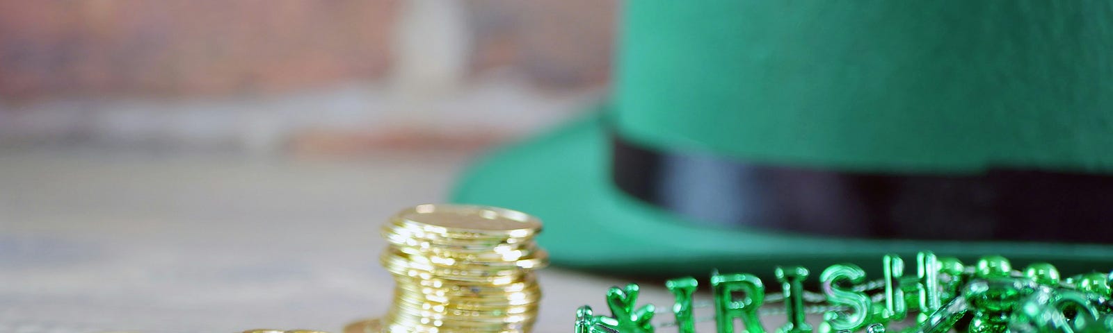 Green felt hat, shamrock necklace, and plastic gold coins on a table top.