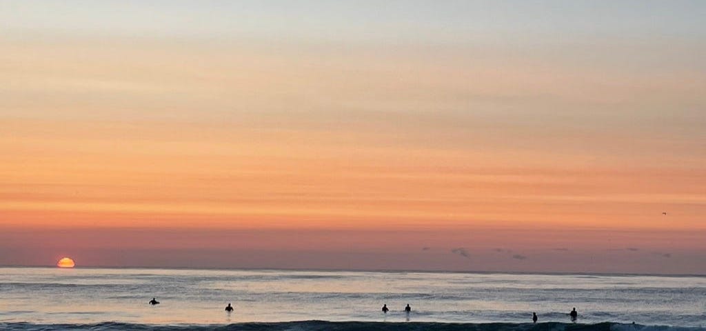 Six surfers pause to watch the sunrise on a late August morning