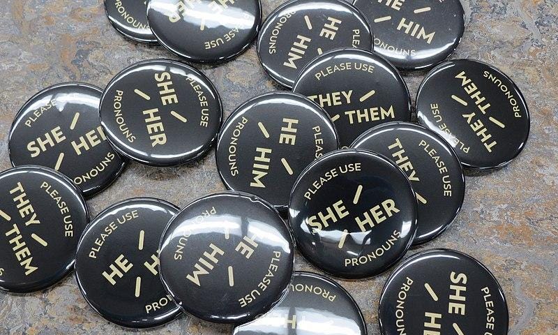 A cluster of pronoun buttons that read, “Please Use She/Her, He/Him, or They/Them Pronouns”