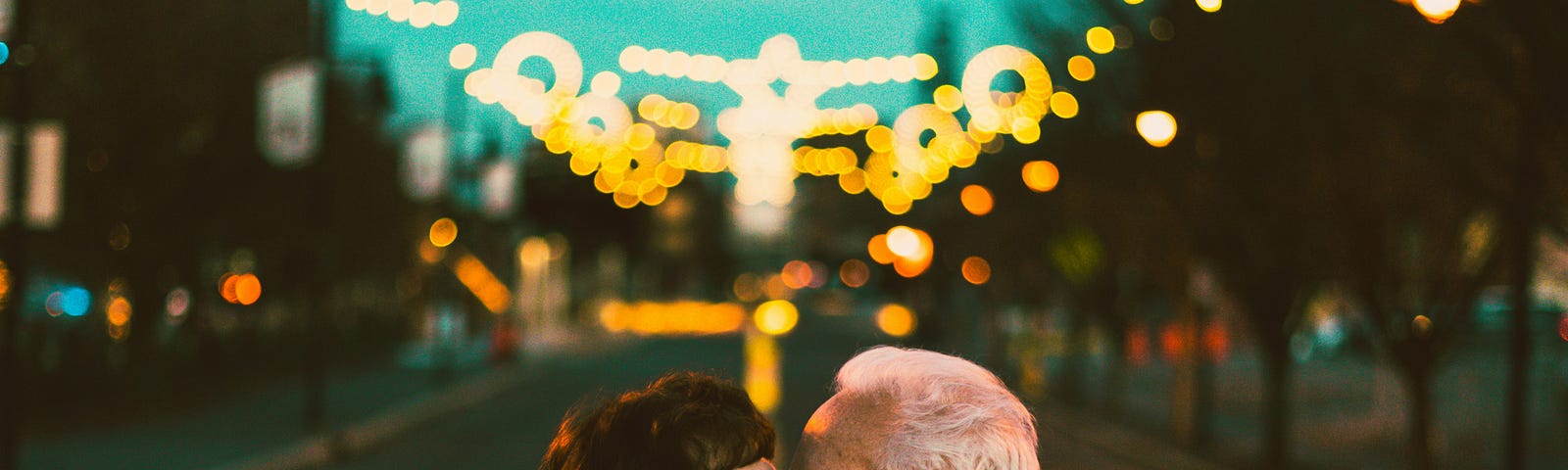 An older couple kissing under stringed lights.