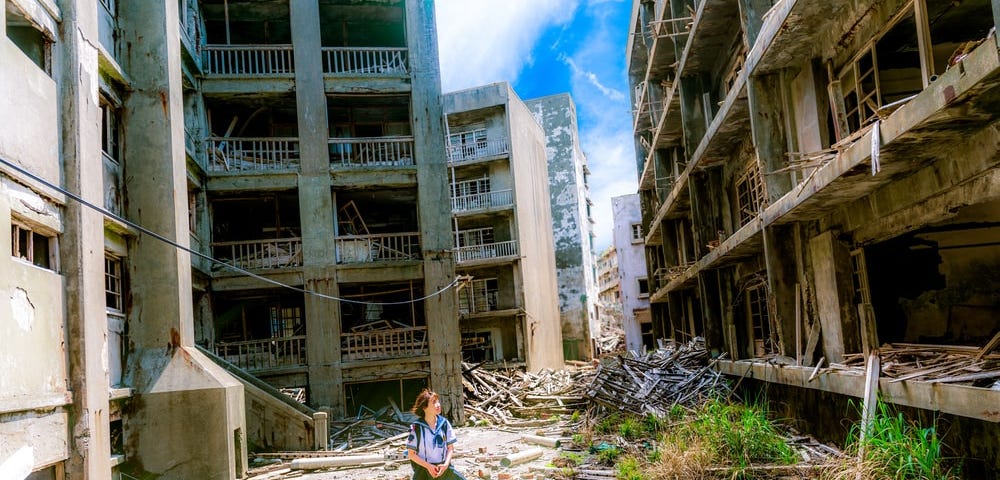 A young girl walks between two blocks of derelict buildings in a war-torn zone