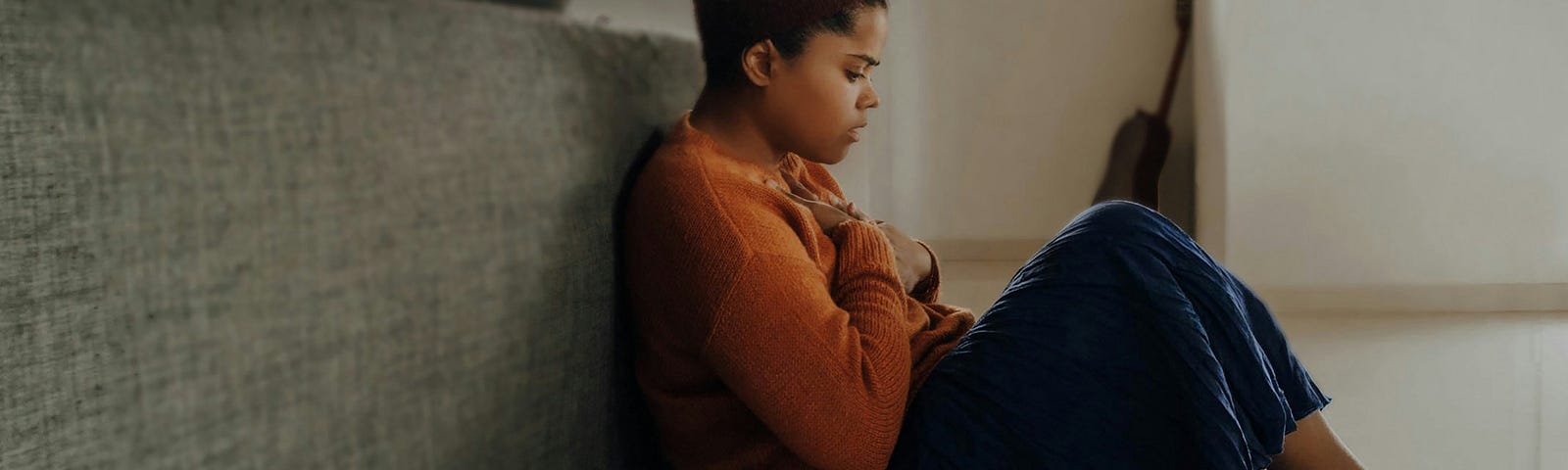 A girl sitting on the floor behind a couch and looking sad or anxious.