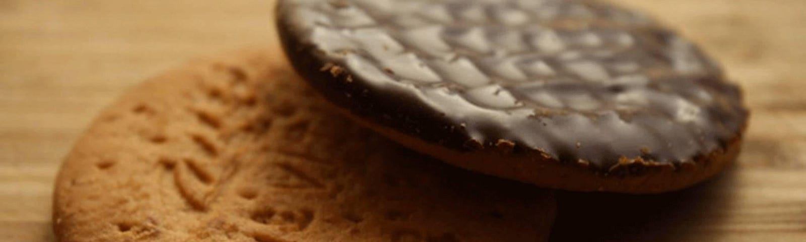 Two chocolate digestives, one placed at a jaunty angle on the lip of another.