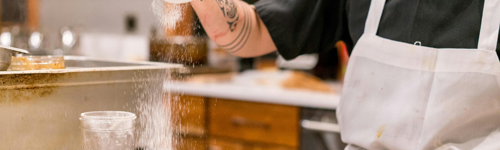 A baker distributes icing sugar over small pastries.