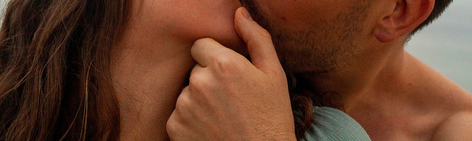 Man and woman kissing. He’s holding her chin and kissing her from behind.