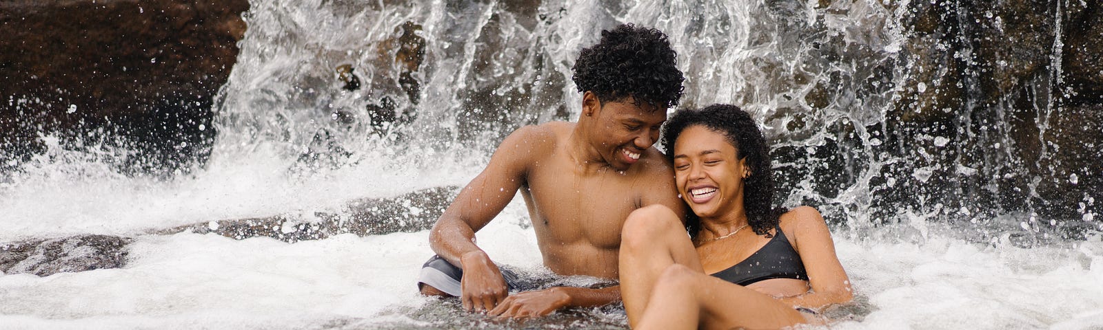 A couple in the water, near a waterfall