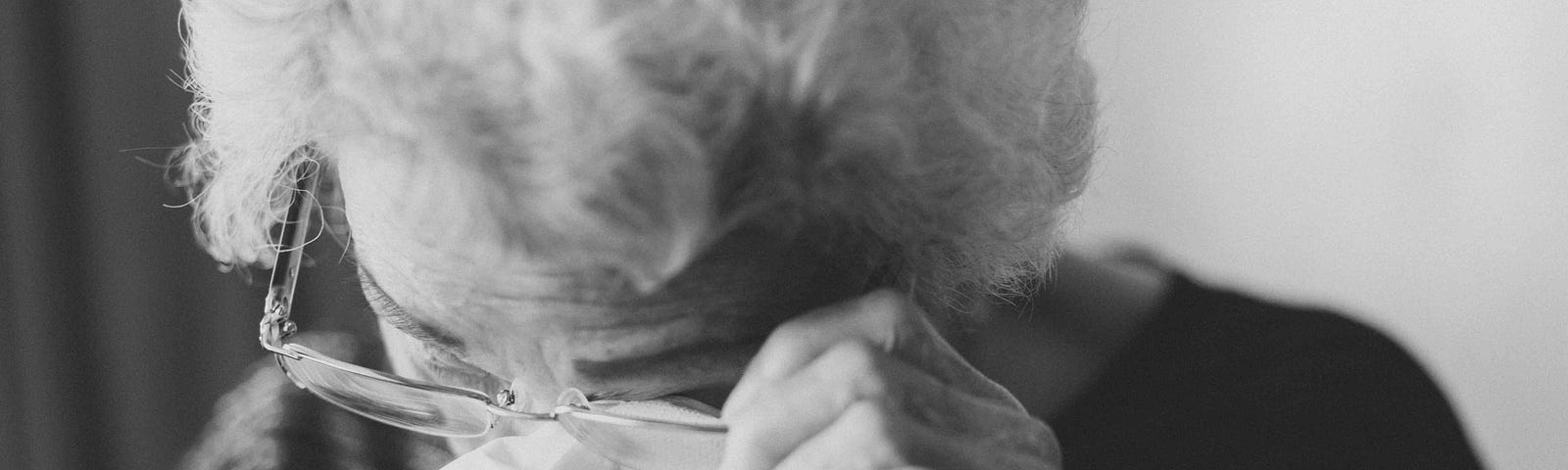 An elderly woman wipes her eyes with a tissue.