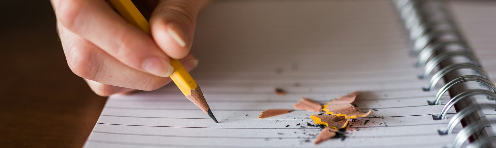 A hand writing in a note book with a yellow pencil.