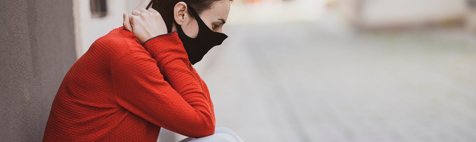 A woman sits outside with a mask on.