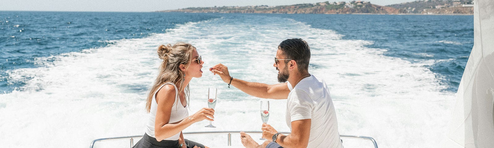 Couple on the back of a motor yacht in the islands, drinking champagne.