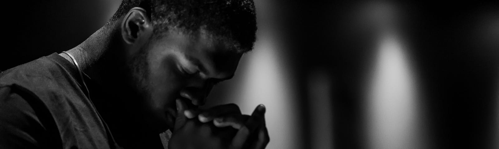 A young man in a dark room, deep in prayer.