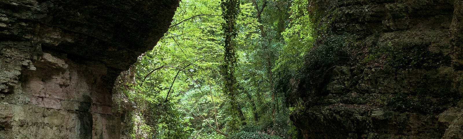 A Women traveller with a back pack, walking in a jungle, in water facing a two large rocks and in th middle the green of the forest