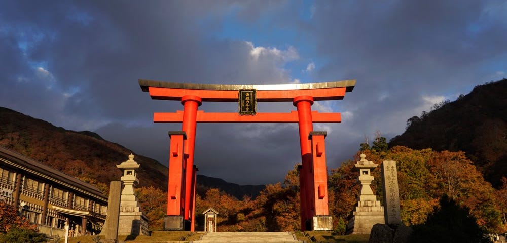 Bright vermillion torii shrine gates of Mt. Yudono shined on dominate the frame with a dramatic dark blue sky in the background