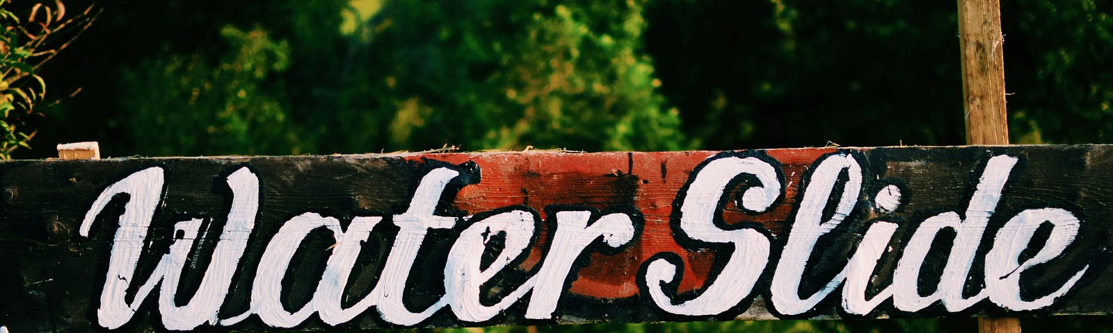 A wooden sign, boldly painted in big white cursive letters, reads “Water Slide.”