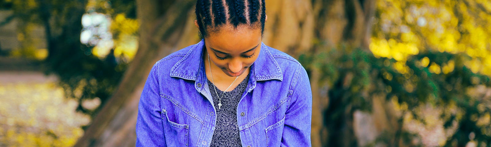 a balck woman dressed in bright blue sits by a tree, writing in her hournal.