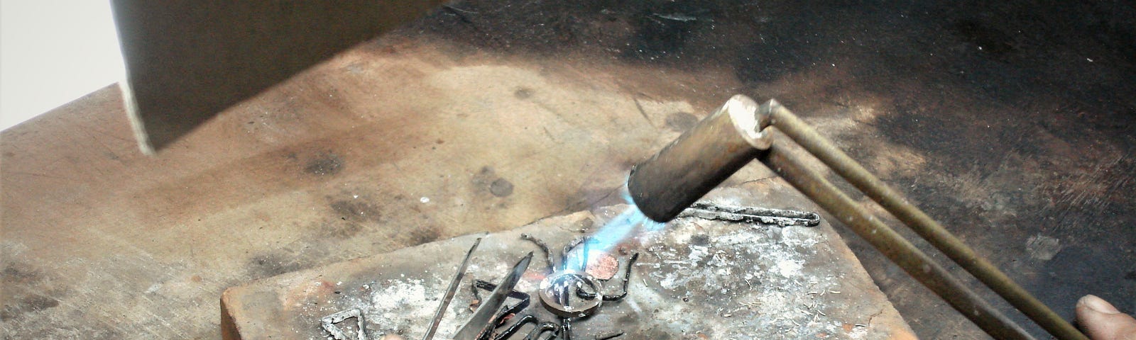 A close up image of a soldering block where a jeweler is in the process of torch-soldering a ring.