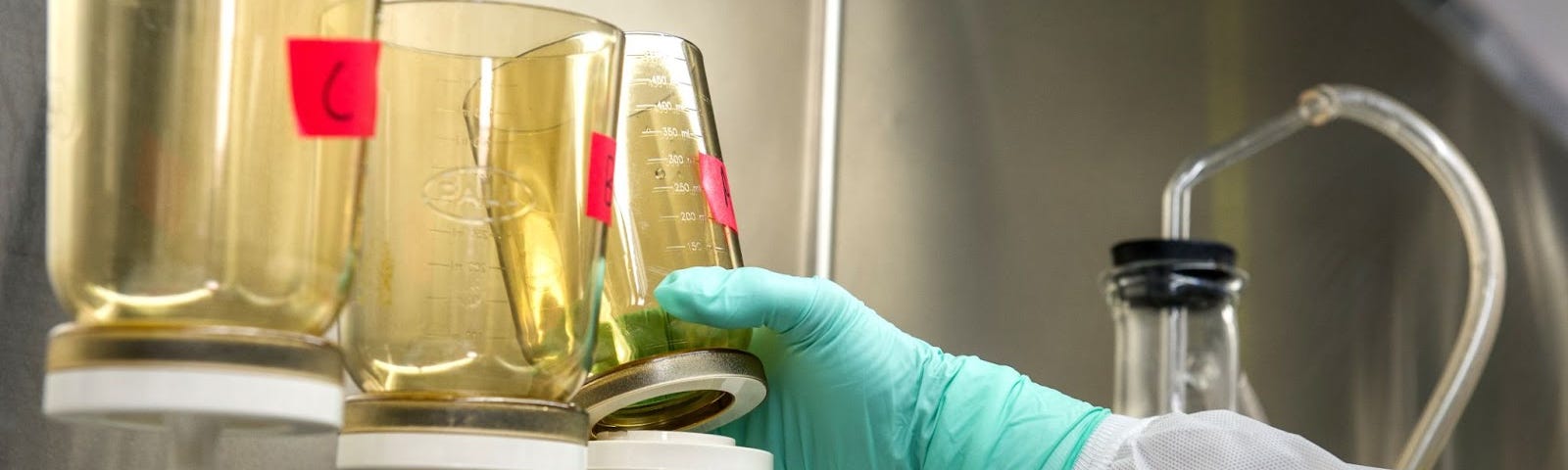 Scientist reaching for beaker of chemicals in laboratory (PFAS, PFOA)