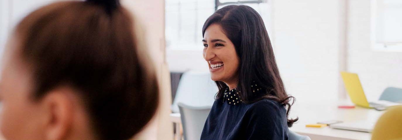 Photo of two women in business attire who are laughing while sitting in their office.