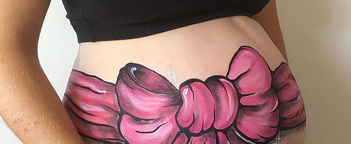 A woman’s pregnant belly painted with a big pink bow.