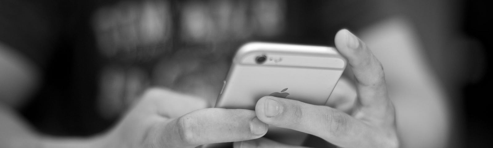Two hands in close up hold an iPhone. The rest of the user’s body is blurred.