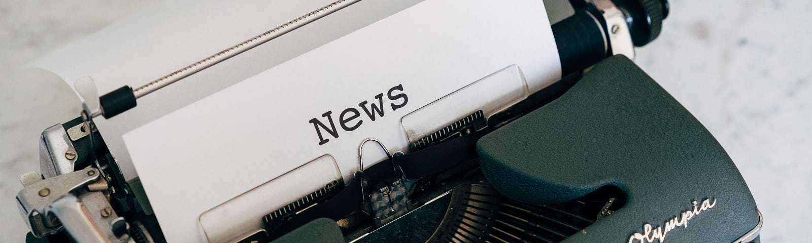 Dark green modern typewriter with a piece of paper in it that has the word “news” typed on it in typewriter font