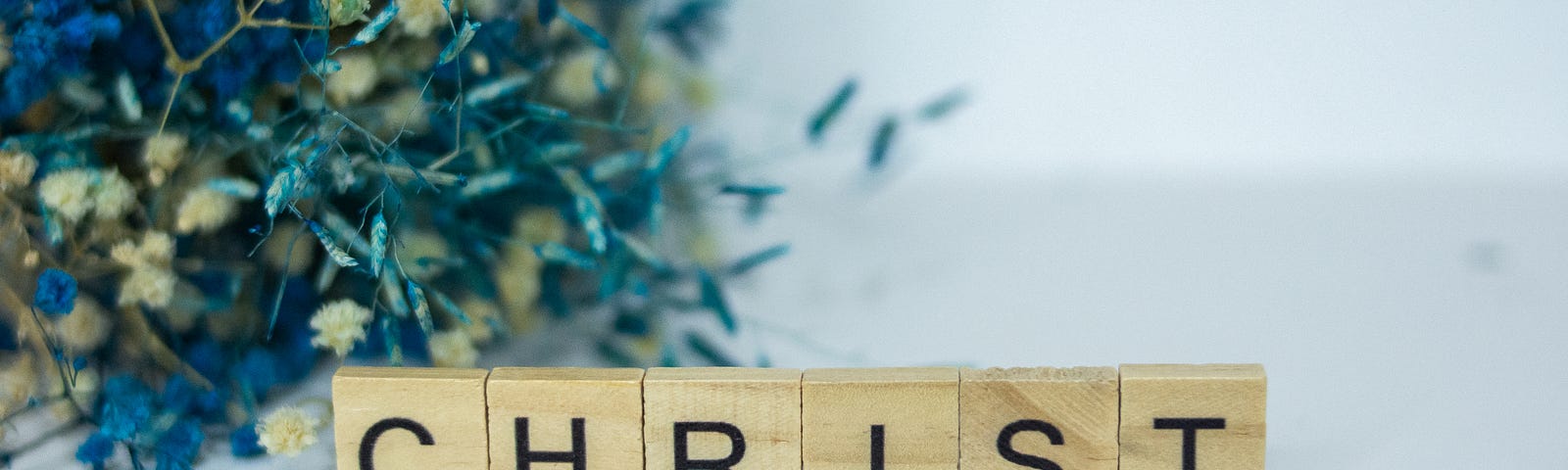 Scrabble tiles that spell CHRIST on white surface with baby’s breath flowers.