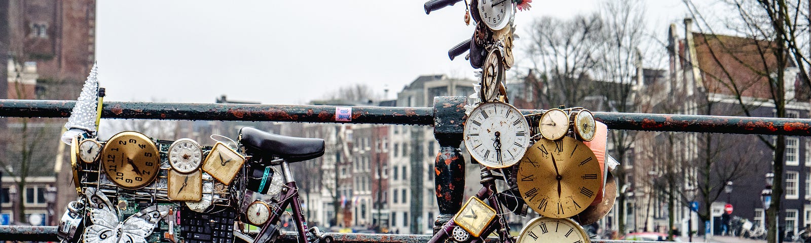 Bicycle covered with clocks, parked on a low bridge over a canal
