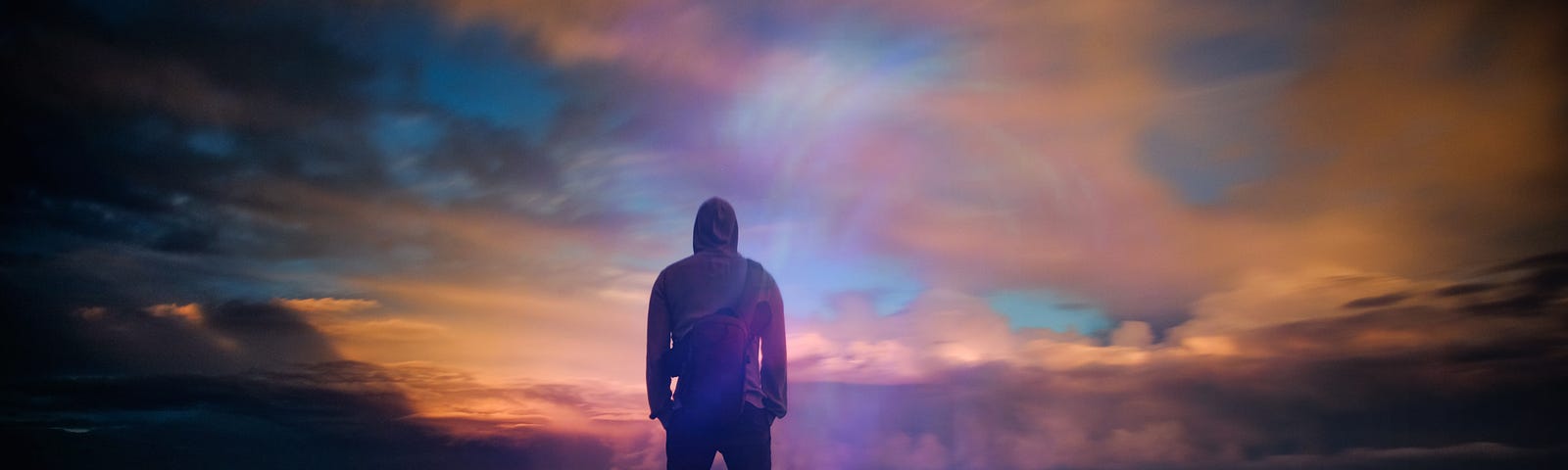 Man in hoodie looks out to the twilight horizon.