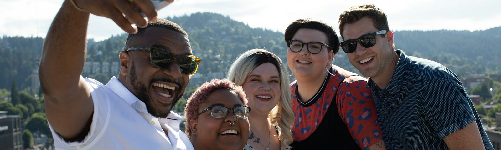 Five people taking a selfie, with mountains in the background.