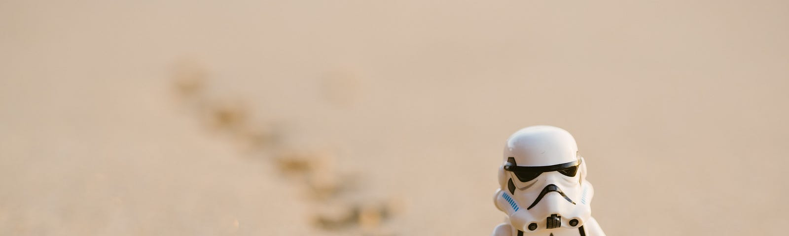 Photo by Daniel Cheung of a Lego Stormtrooper walking through the sand with footsteps behind him.