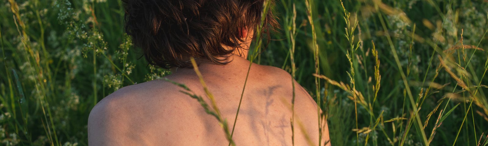 Self portrait of a woman and her mental health in the grass with her back to the camera.