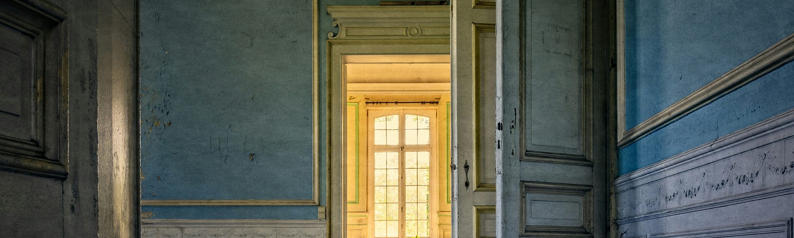 A beautiful old abandoned house, sunlight shining through a window at the end of a gray series of open doors.