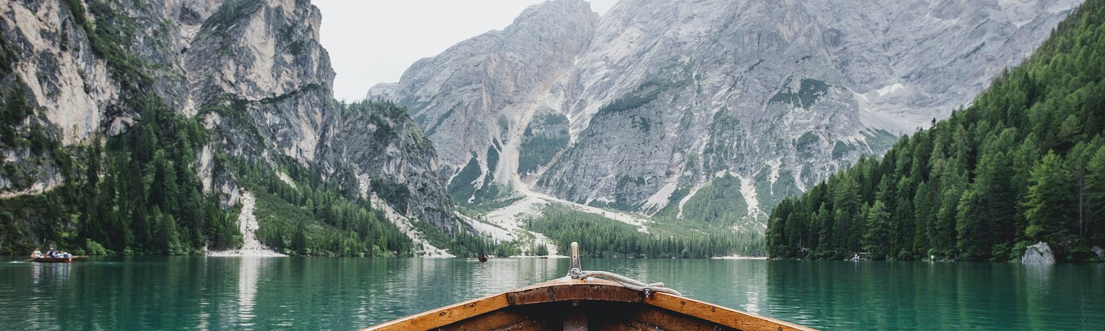 A wooden boat floating in green waters facing a beautiful mountain