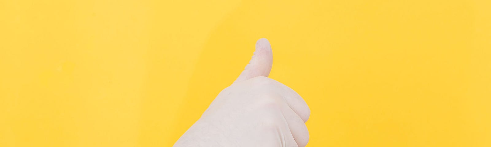 A hand with a latex glove making the thumbs-up sign, over a yellow background