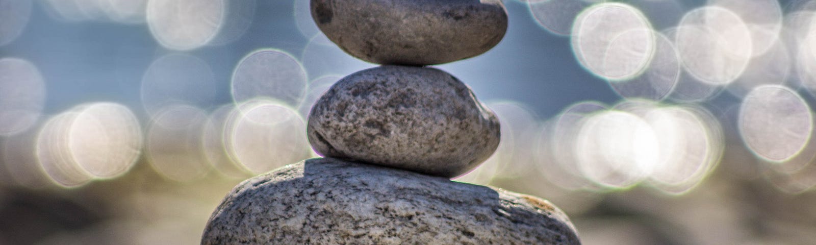 Rocks stacked tall to show balance with a scene from a lake behind it unfocused.