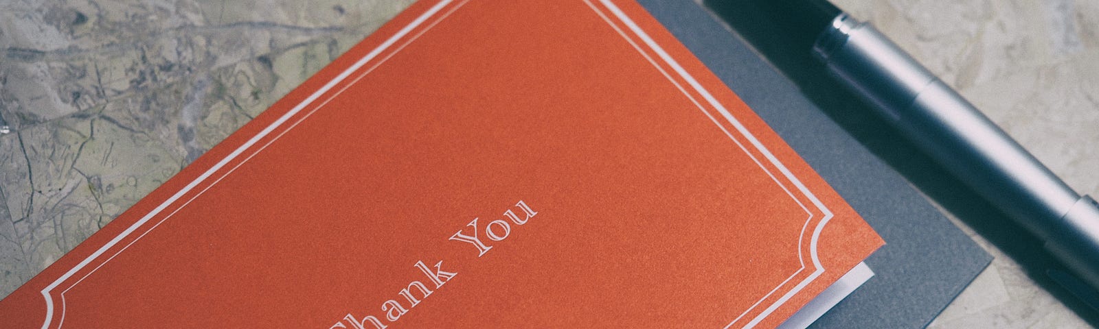 A formal card with Thank You printed on the cover, next to a fountain pen. This will soon be a thank you letter.