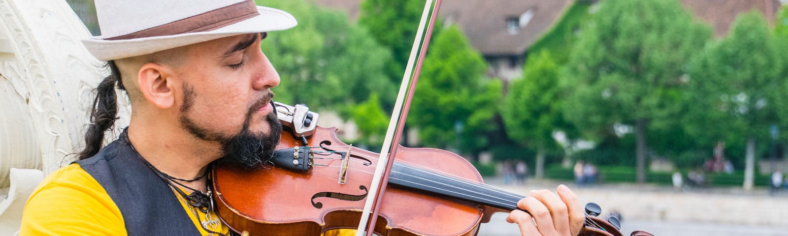 a man with a ponytail and a white hat, playing the fiddle