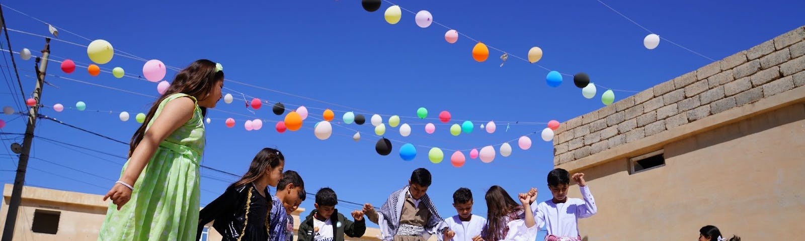 Children gather outside at a child-friendly space under balloons.