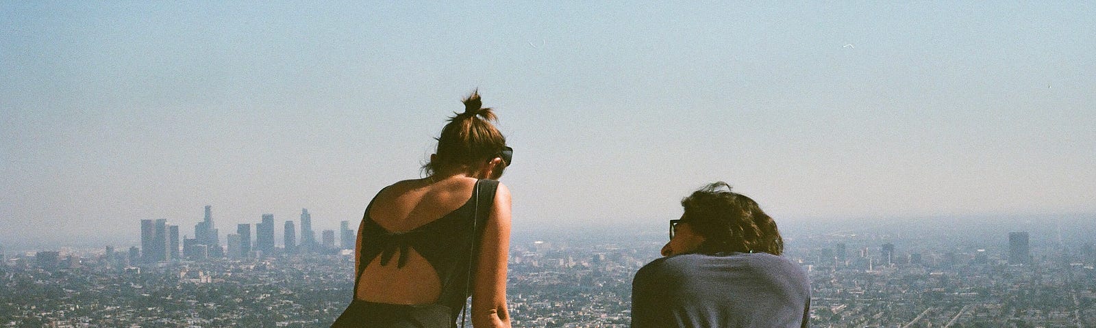 Woman and male on a platform or hill overlooking a city skyline in summer.